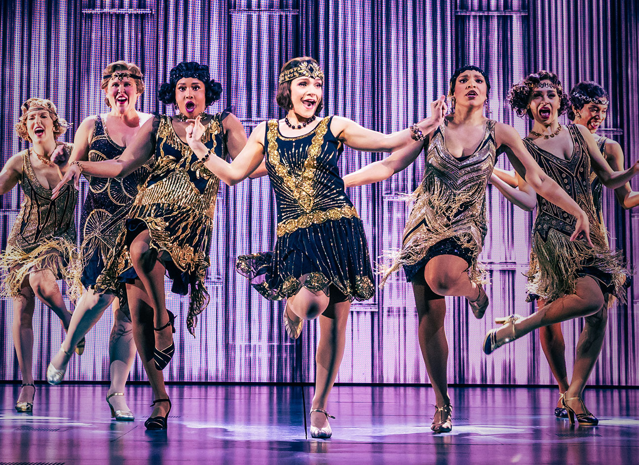 Jeremy Jordan and Eva Noblezada as Jay Gatsby and Daisy Buchanan embrace on a dance floor, at an extravagant party, looking into each other's eyes very seriously